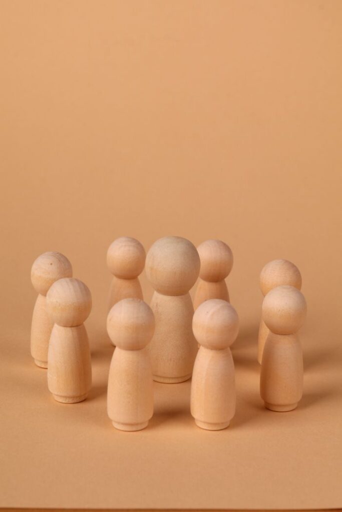 Group of minimalist wooden figures forming a circle on a beige background, symbolizing community or teamwork.